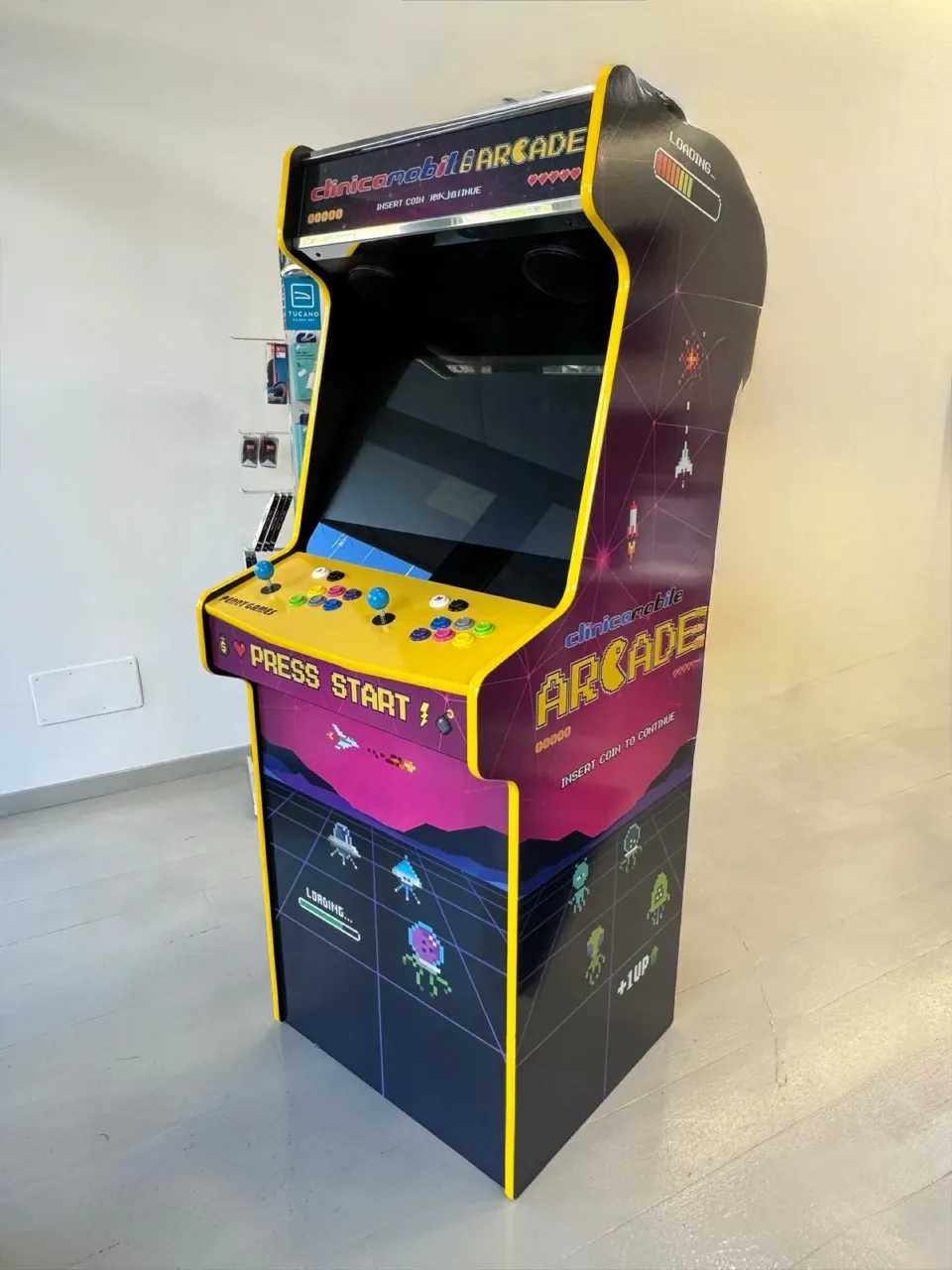 Il cabinet visto di tre quarti: marquee, pannello comandi giallo, frontale con astronavi e alieni e il fianco con la scritta Arcade