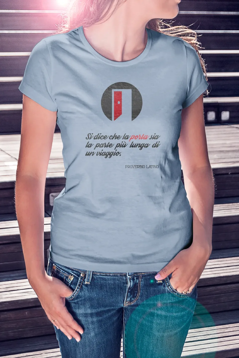 Maglietta azzurra con la porta del Circolo Aurora e la frase: Si dice che la porta sia la parte più lunga di un viaggio, proverbio latino
