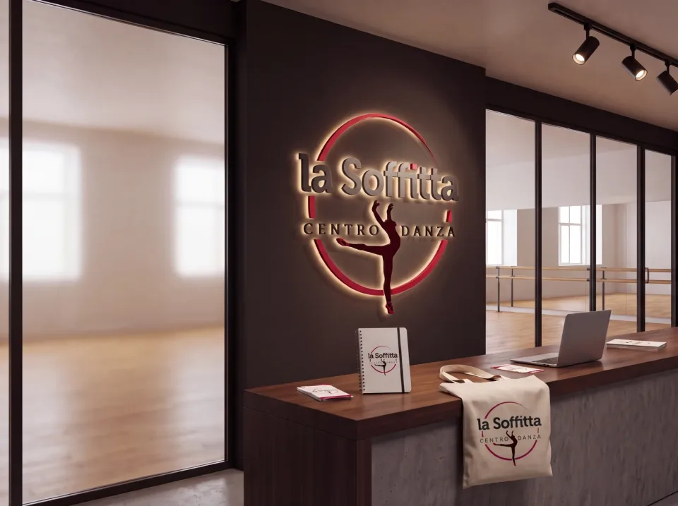 Il marchio La Soffitta Centro Danza come insegna luminosa sulla parete scura di una reception, con quaderno, borsa di tela e pieghevoli sul bancone