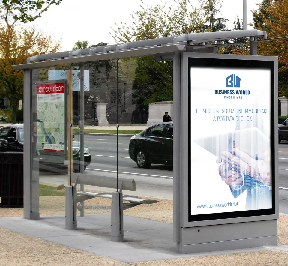 Manifesto Business World in una pensilina dell’autobus: il marchio, la frase Le migliori soluzioni immobiliari a portata di click e l’indirizzo del sito